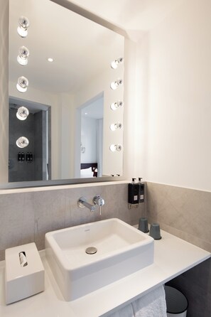 Un baño moderno con un espejo grande, varias luces, un lavabo y artículos de aseo.