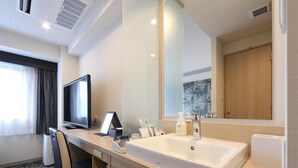 Ein Hotelzimmer mit einem großen Bett, einem Schreibtisch mit Computer, einem großen Spiegel und einem Waschbecken.