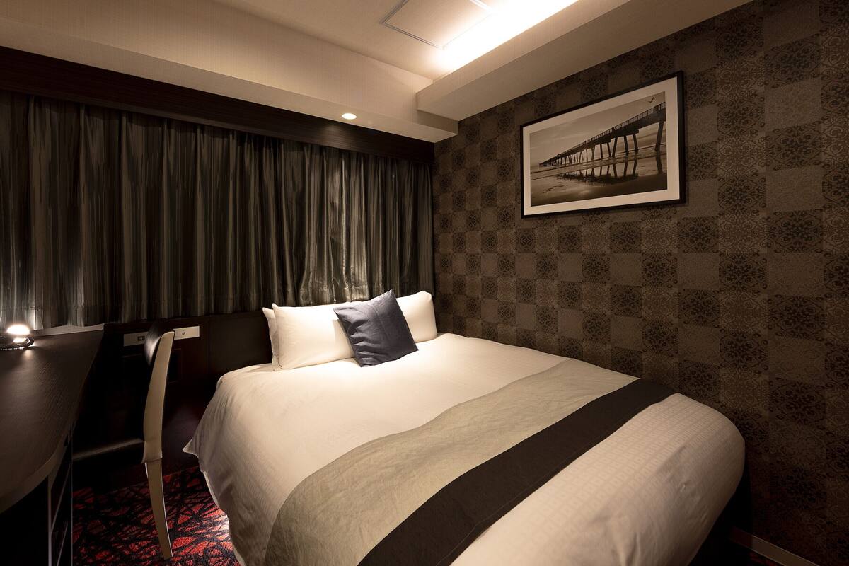 A hotel room with a large bed, a desk, and a chair.