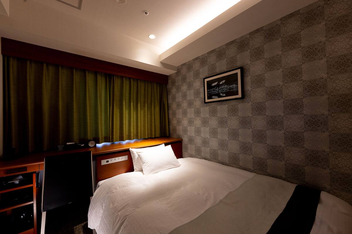 A hotel room with a bed, a desk with a computer, a chair, and a wall with a patterned design.