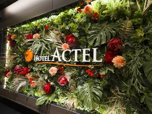 Un mur orné d’une composition florale et sur lequel on peut lire le texte « HÔTEL ACTEL ».