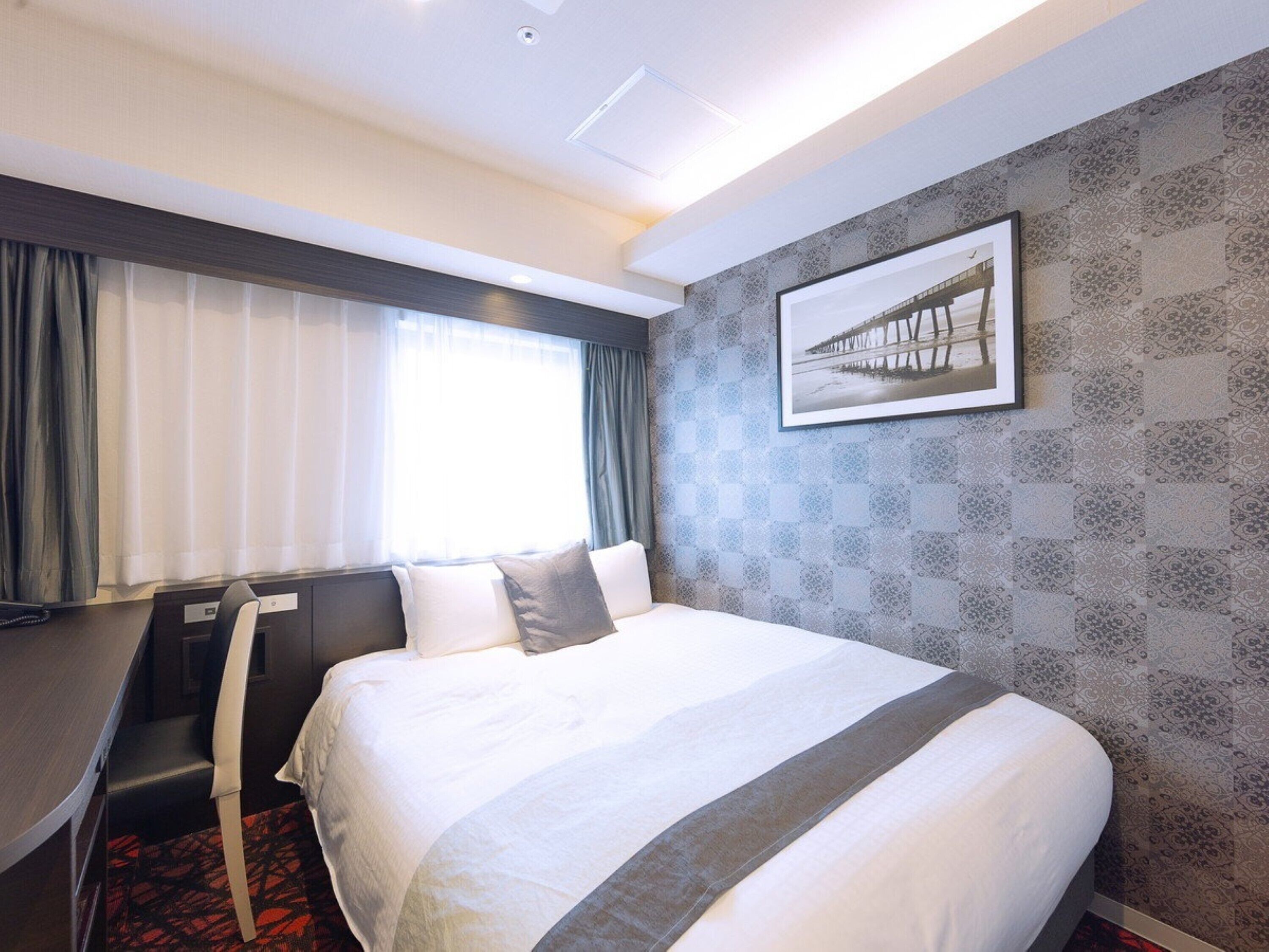 A hotel room with a bed, a desk, and a chair.