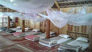 Una habitación con varias camas, cada una con mantas y almohadas ordenadas, y una cama con dosel y mosquitero.
