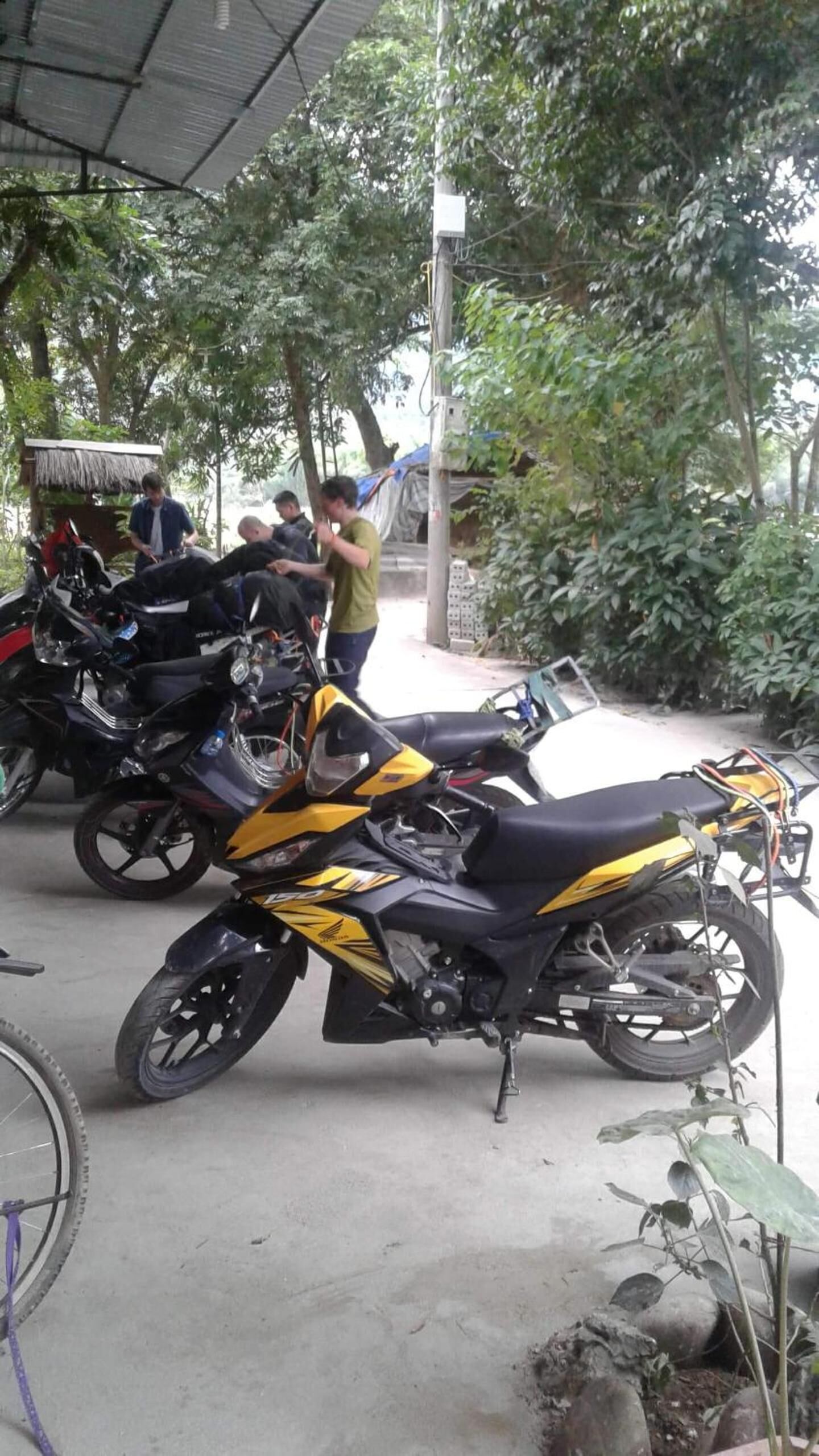 Une moto est garée à l’extérieur, avec une structure à toit de chaume en arrière-plan.