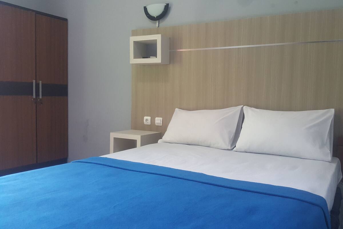 A bedroom with a bed, a nightstand, a wall-mounted light, and a wardrobe.