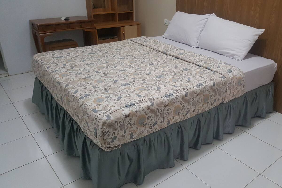 A bed with a floral bedspread and a green skirt, a wooden headboard, and a small wooden desk with drawers.