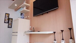 A modern living room with a mounted TV, white shelves, decorative vases, and a potted plant. - Metro Malioboro Living (Yogyakarta)