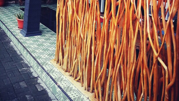 A covered outdoor area with a patterned floor, a column, and a decorative wall made of orange sticks. - Metro Malioboro Living (Yogyakarta)