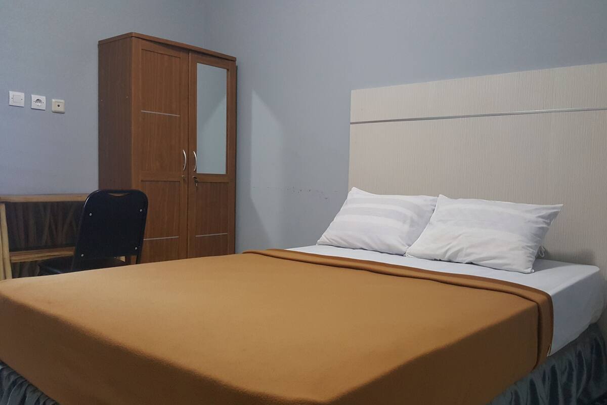 A bedroom with a bed, a wooden wardrobe, a desk, and a chair.