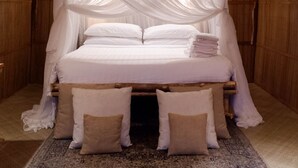 Un lit à baldaquin en bois, avec des draps et des oreillers blancs, une tête de lit en bois et un tapis à motifs sur le sol.
