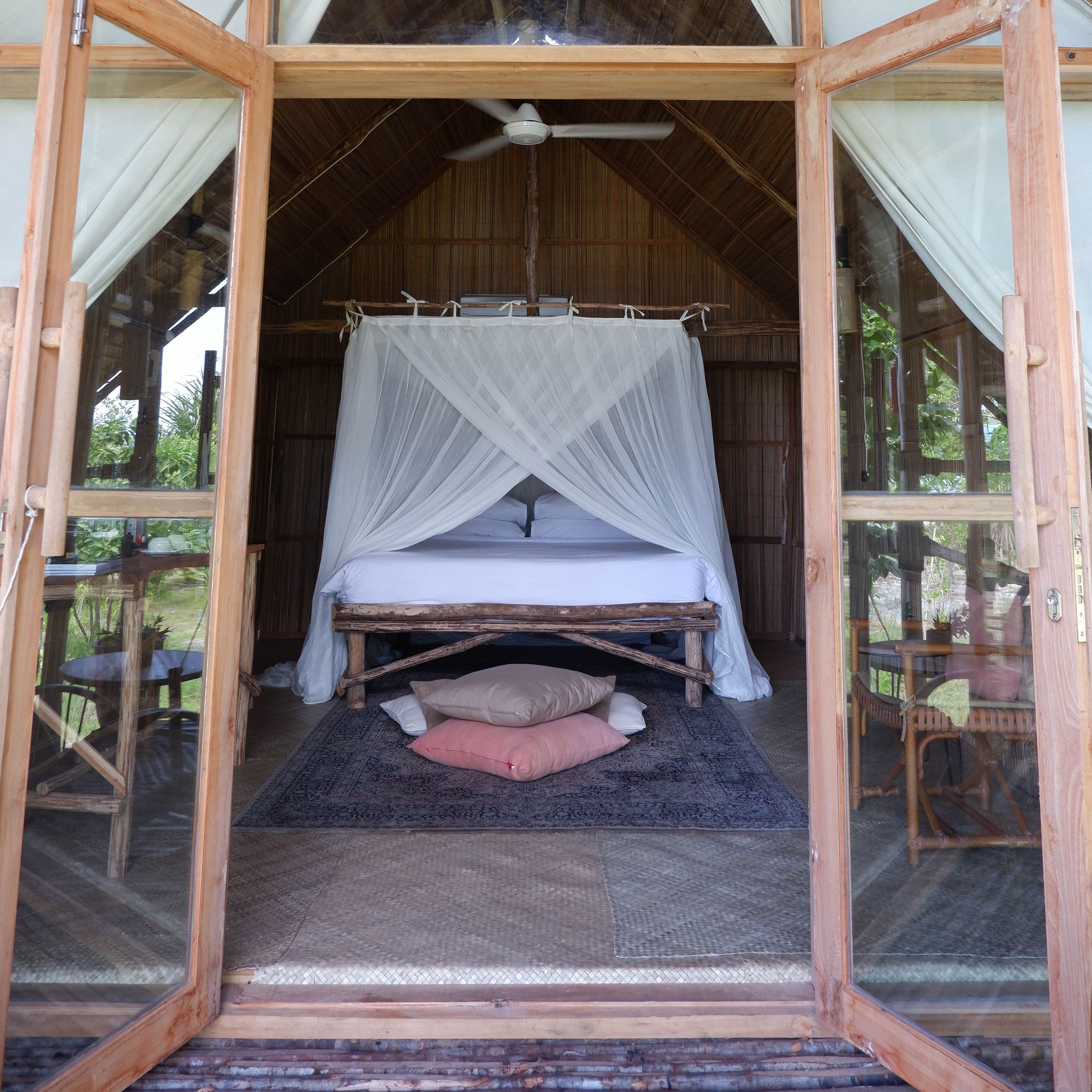 A wooden-framed room with a bed, a ceiling fan, and a mosquito net.