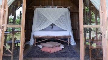 A wooden-framed room with a bed, a ceiling fan, and a mosquito net.