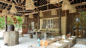 Un coin repas rustique avec une longue table en bois dressée pour le repas, entouré de lampes suspendues en fibres tressées et d’un plafond en bois rustique.
