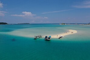 Une mer d’un bleu turquoise limpide, une plage de sable, des bateaux et une petite île au loin.