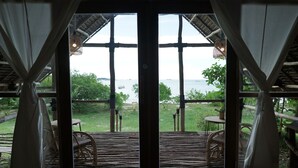 Une terrasse en bois, dotée de chaises et d’une table en osier, qui offre une vue sur une étendue d’eau et sur la verdure.