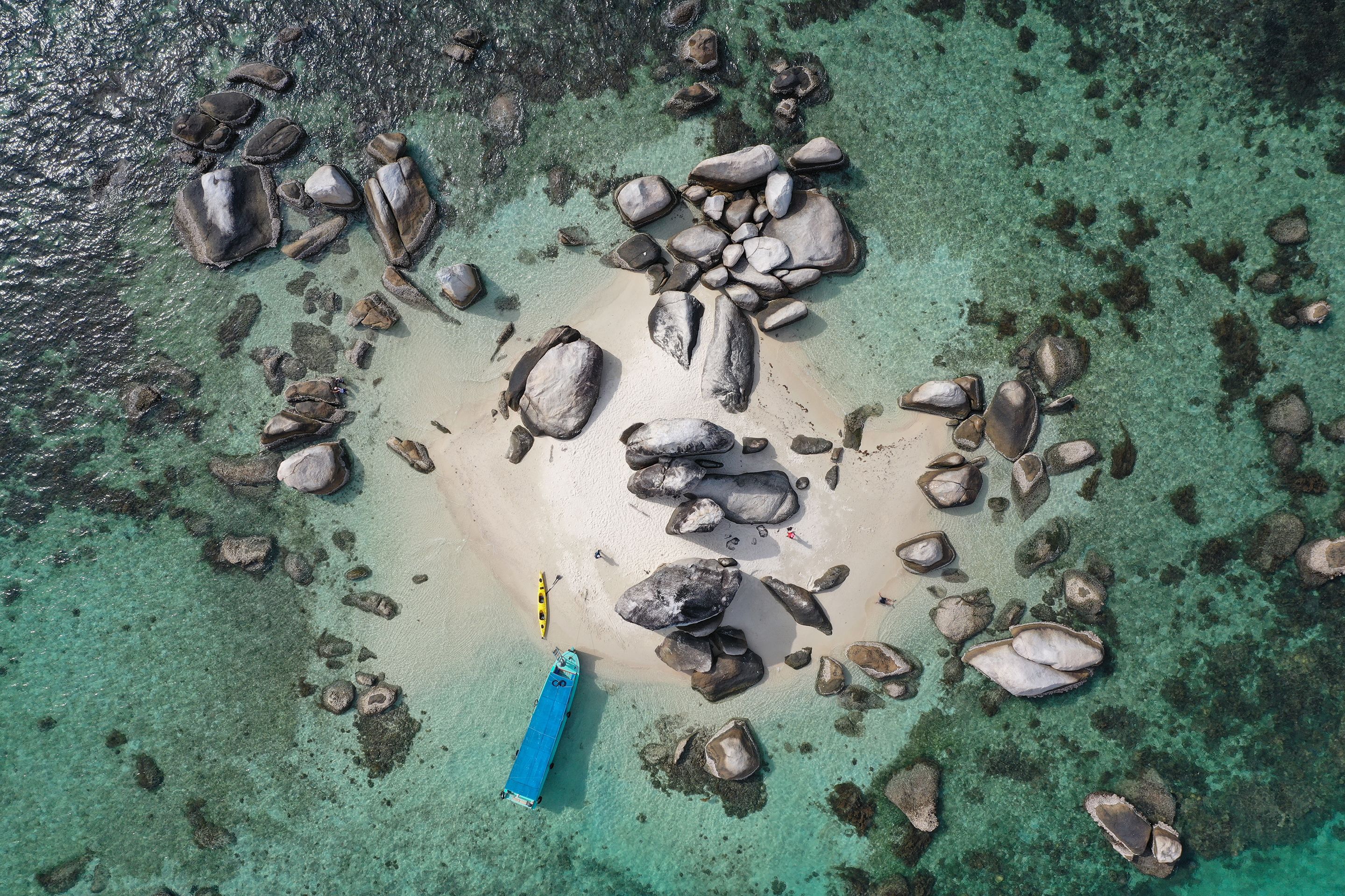 An aerial view of a beach with scattered rocks and a blue boat.
