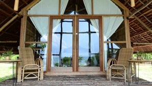Un espace extérieur aménagé, abrité et doté de chaises en osier et d’une table, de grandes portes vitrées donnant sur une vue imprenable sur la mer, et d’une structure de plafond en bois.