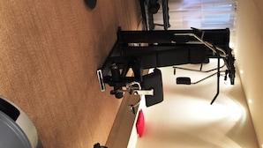 A stationary exercise bike with a digital display, a wall-mounted control panel, and a window with blinds in the background.