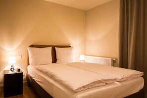 A neatly made bed with white linens, two bedside lamps, and a radiator under the headboard. - Mondrian Suites Hotel Berlin Checkpoint Charlie (Berlin)