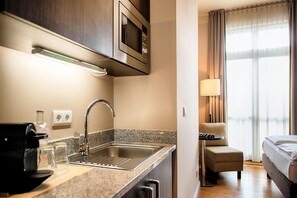 A hotel room with a kitchenette, including a microwave, sink, and coffee maker. There is a bed, a chair, and a lamp. - Mondrian Suites Hotel Berlin Checkpoint Charlie (Berlin)