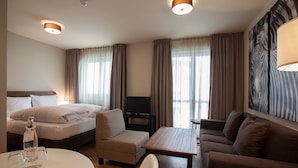 A hotel room with a bed, a sofa, a small table, a TV, and a painting on the wall.