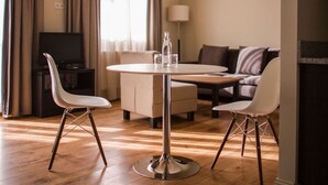 A hotel room with a round dining table, two white chairs, a sofa, a TV, and a lamp.