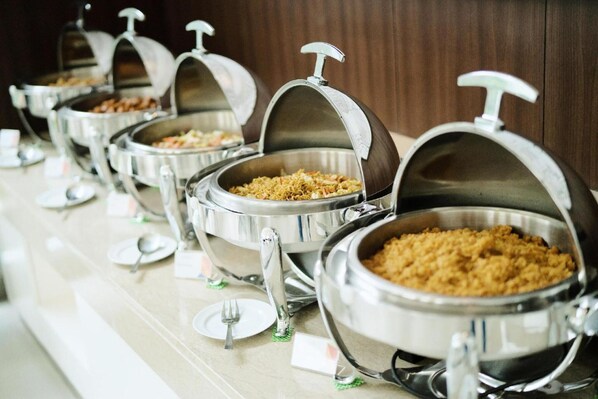 A buffet line with multiple self-service food stations, each with a metal dome cover and a spoon on the counter.