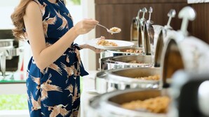 A woman in a blue dress with a bird pattern standing in a modern kitchen with multiple serving stations. - Amaris Hotel Fachrudin – Tanah Abang (Jakarta)