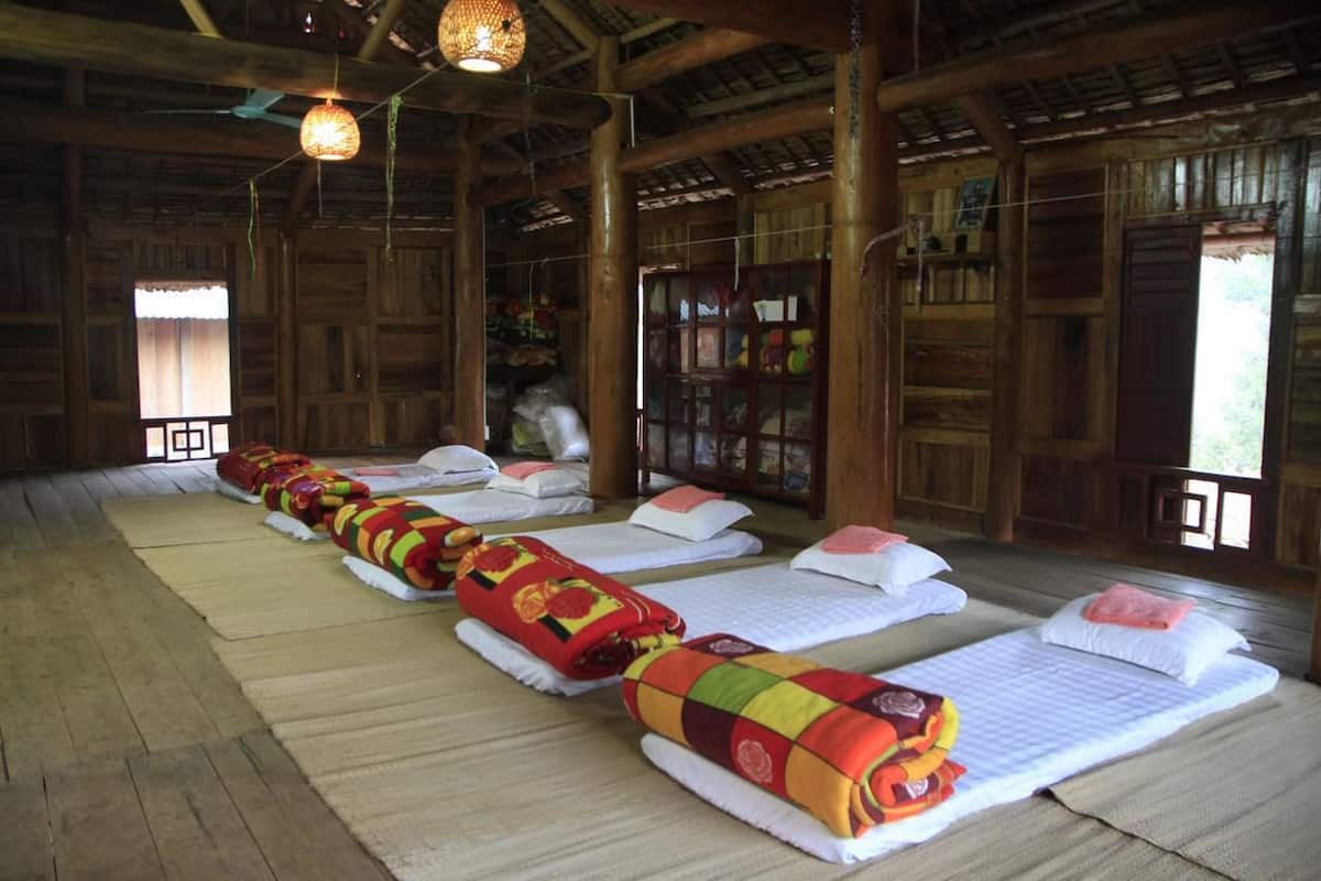 A room with wooden walls and floors, multiple beds with colorful blankets, and a hanging light fixture.