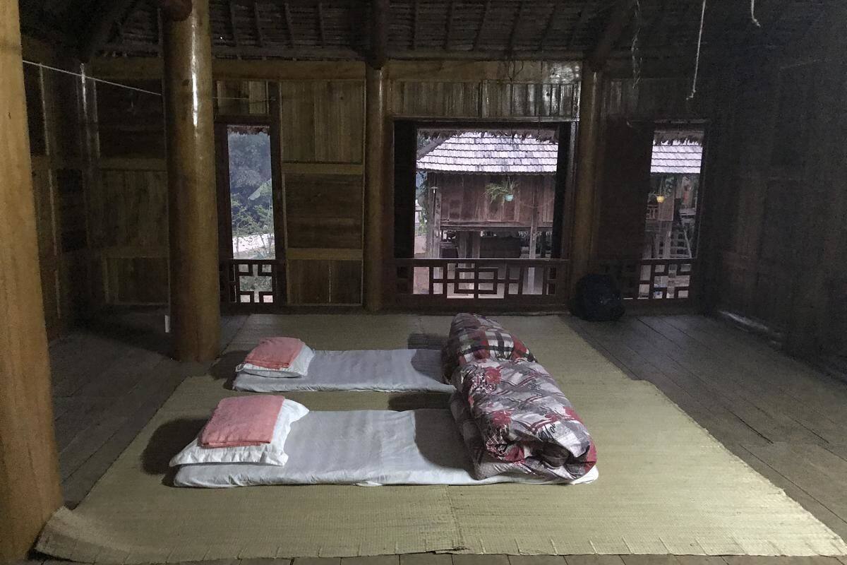 A traditional wooden room with two beds, a mat on the floor, and a view of a mountain through a window.