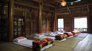 A traditional wooden room with multiple beds arranged in a row, large windows, and a ceiling fan. - Ban Buoc Homestay - Hostel (Muong Bi)