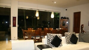 A modern living room with a white sofa, black and white patterned cushions, a dining area with wooden chairs, and pendant lighting. - Villa Pantai Lovina (Kubutambahan)