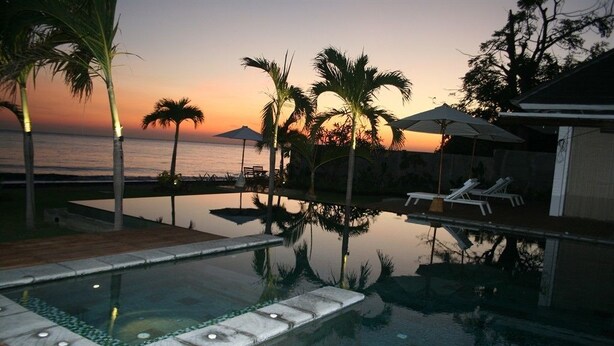 A swimming pool with a wooden deck, palm trees, and lounge chairs. - Villa Pantai Lovina (Kubutambahan)