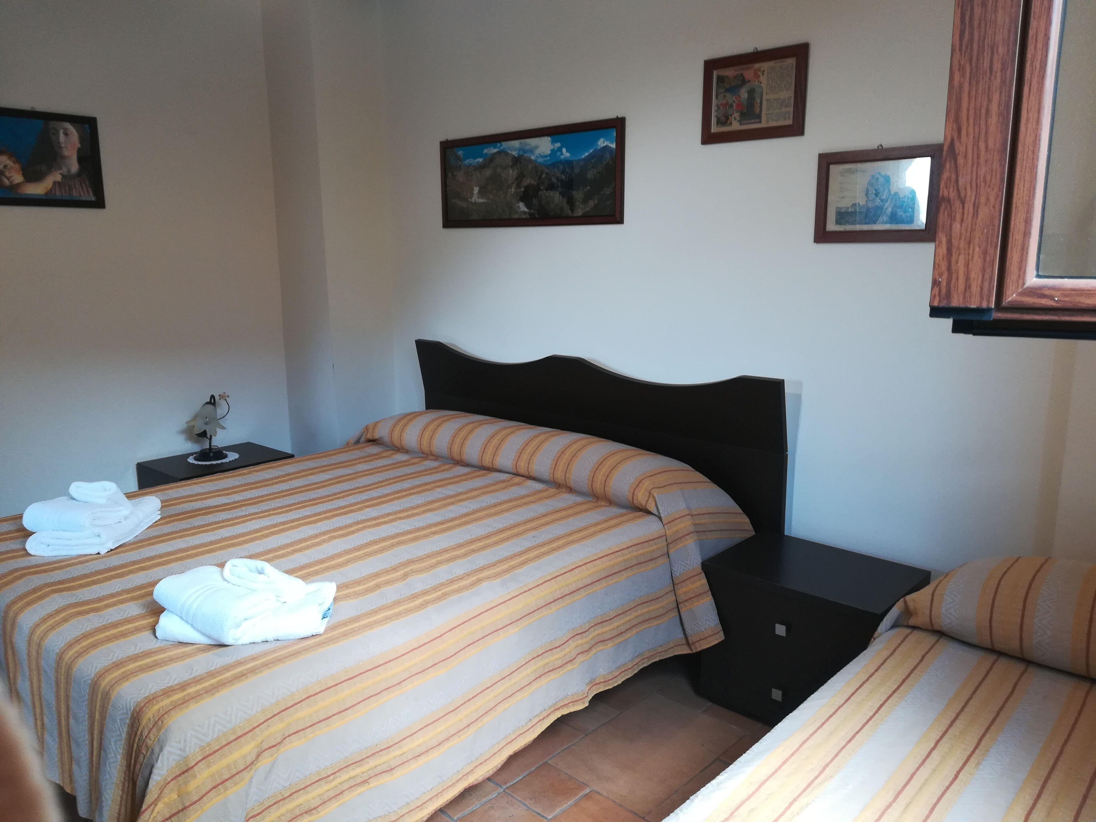 Habitación de hotel con dos camas, una mesita de noche y una pared decorada con cuadros.