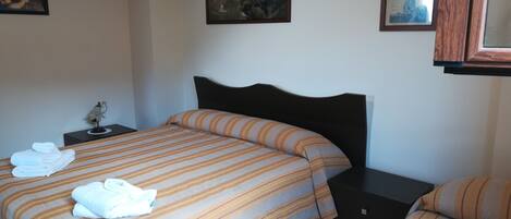 Habitación de hotel con dos camas, una mesita de noche y una pared decorada con cuadros.