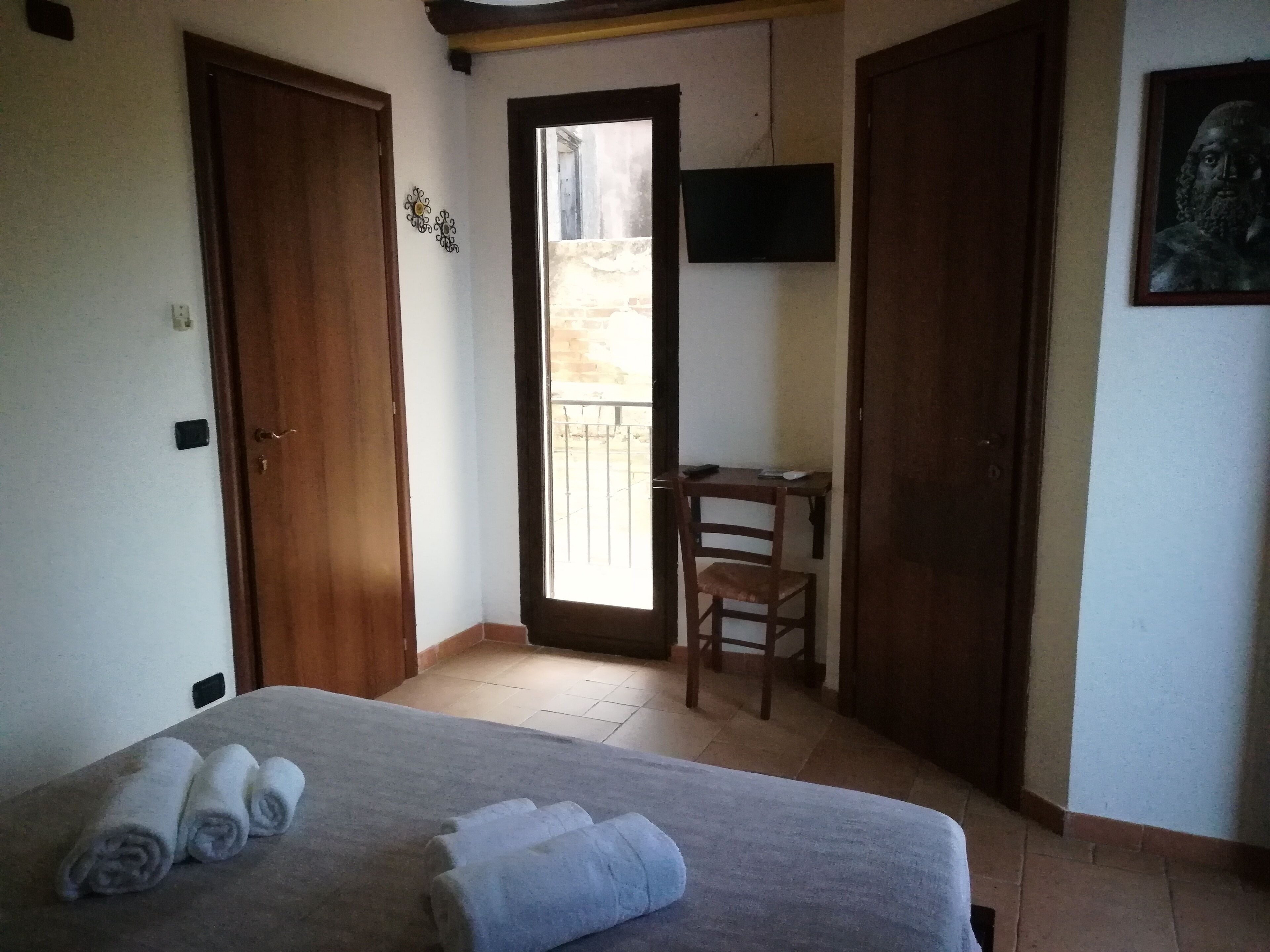 A bedroom with a bed, two doors, a chair, a TV, and a balcony.