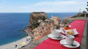 A coastal town with a historic fort overlooking the sea, a red mat with cups and pastries, and a clear view of the beach and buildings. - B&B La Bastia  (Scilla)