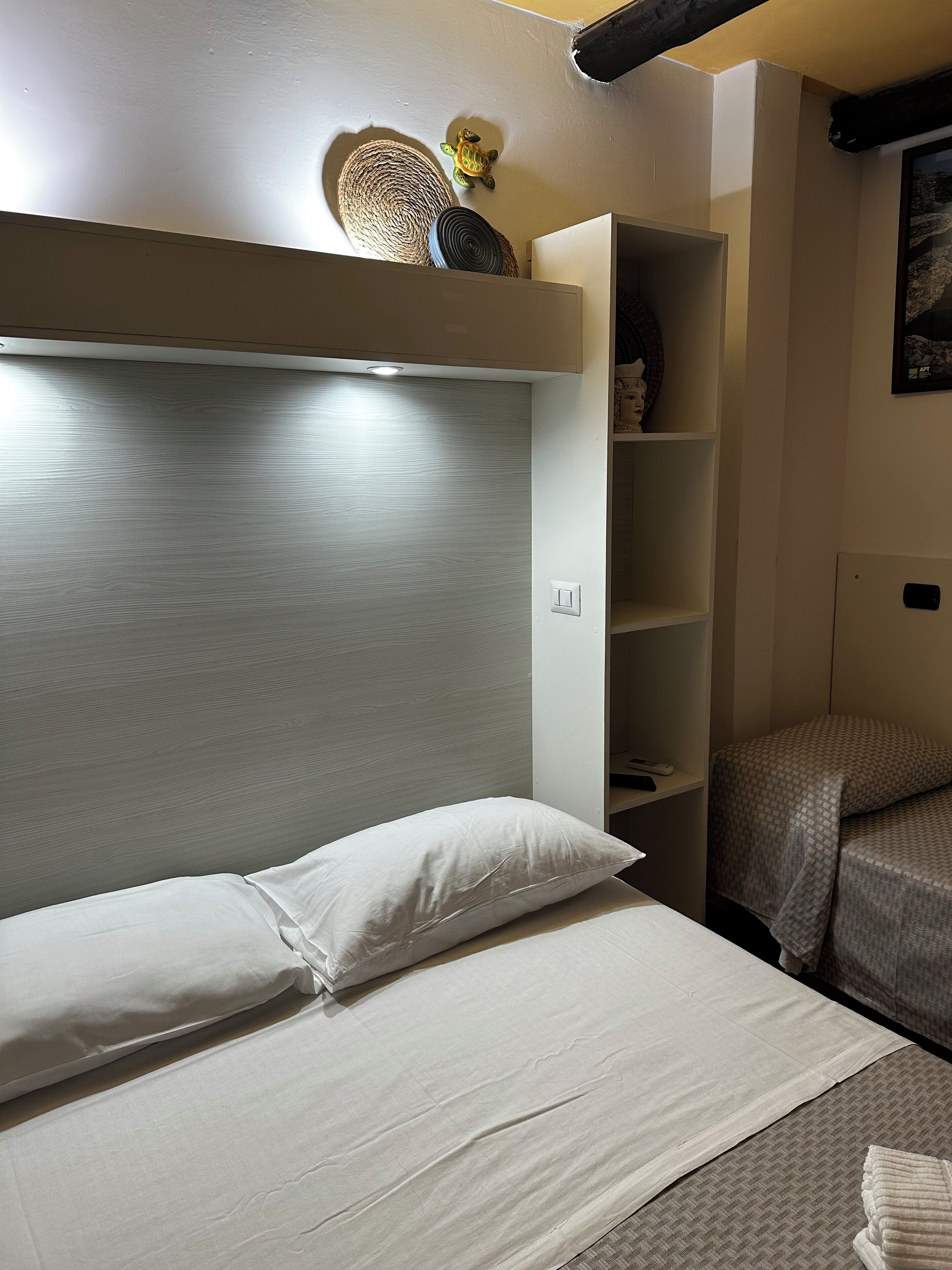 A bedroom with a bunk bed, a headboard, a shelf with decorative items, and a wall-mounted light fixture.