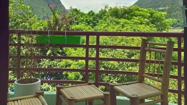 Une terrasse en bois avec deux chaises et une table, offrant une vue sur un paysage verdoyant et luxuriant, avec des montagnes à l’horizon.