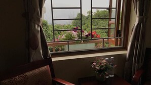 Une pièce avec une fenêtre donnant sur un balcon orné de fleurs. On y trouve une table avec un vase de fleurs et deux chaises.