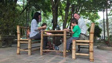 A group of people seated at a bamboo table in an outdoor setting with trees in the background.