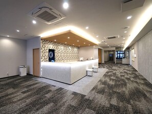 A modern reception area with a central counter, patterned walls, and carpeted flooring. - Utsunomiya Hotel Maruji (Utsunomiya)