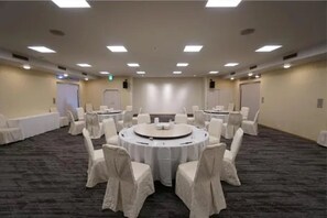 A conference room with a round table surrounded by chairs, a carpeted floor, and a plain wall with a door. - Utsunomiya Hotel Maruji (Utsunomiya)