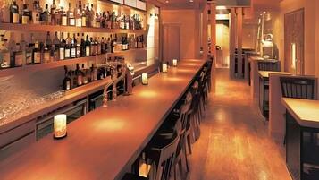 A bar area with a long counter, shelves with bottles, and a few chairs.