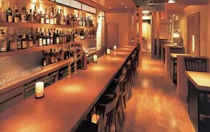 A bar area with a long counter, shelves with bottles, and a few chairs. - Utsunomiya Hotel Maruji (Utsunomiya)