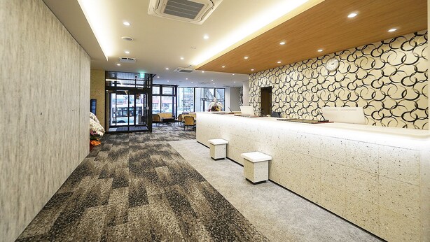 A reception area with a modern design, including a patterned wall, a reception desk, and a carpeted floor. - Utsunomiya Hotel Maruji (Utsunomiya)