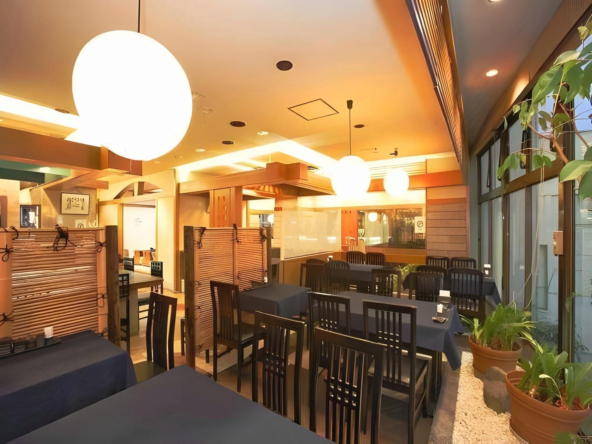 A modern restaurant interior with high ceilings, pendant lighting, and a mix of seating arrangements including tables and booths.