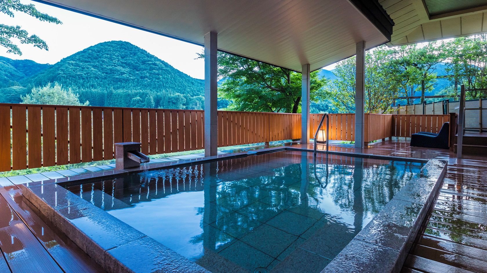 A covered outdoor swimming pool with a wooden deck and a view of a mountainous landscape.