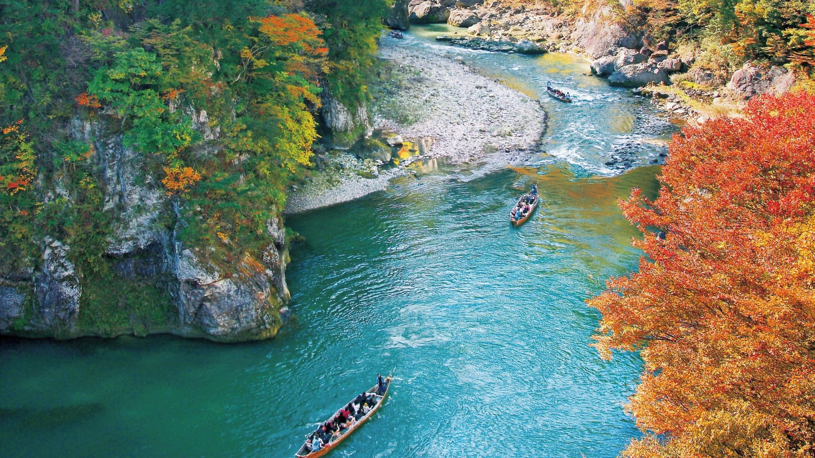 A river with boats, surrounded by rocky cliffs and autumn-colored trees.