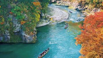 A river with boats, surrounded by rocky cliffs and autumn-colored trees.